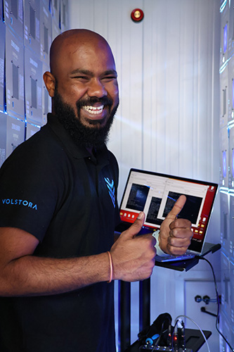 Shyam gives a thumbs up as he stands behind a computer in an energy storage system, programming the batteries 